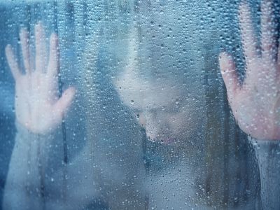 melancholy and sad young  woman  at the window in the rain