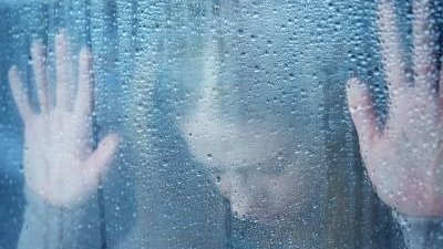 melancholy and sad young woman at the window in the rain